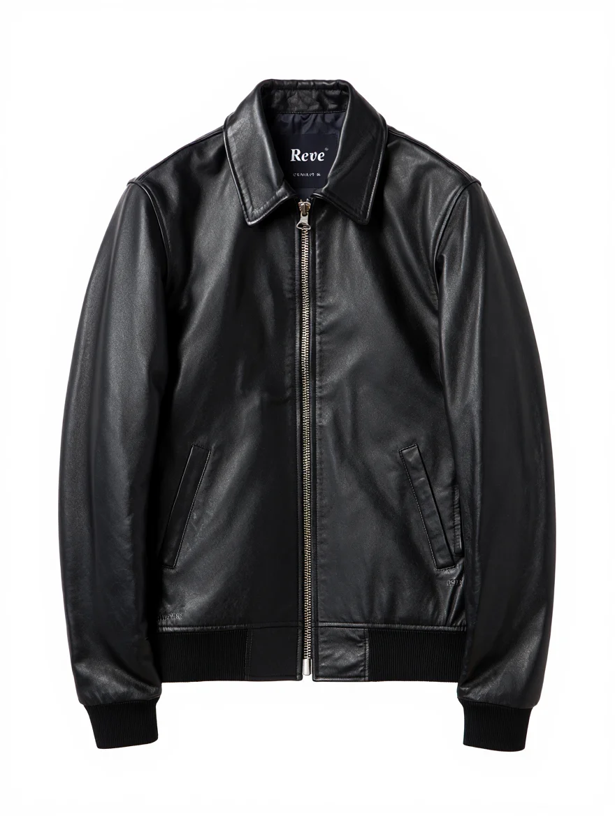 A product photograph captures a classic black leather bomber jacket centered against a pure white background. The jacket features a pointed collar, silver metal zipper front closure, two angled front pockets, and black ribbed knit cuffs and waistband. The leather material displays a distressed, vintage look with subtle sheen under studio lighting. The composition is perfectly centered with even, front-facing artificial lighting that highlights the jacket's premium construction and details. A tag inside the jacket displays the text "Reve" in a distinctive swash font. Professional product photography with studio lighting setup and clean white background composition for commercial use.