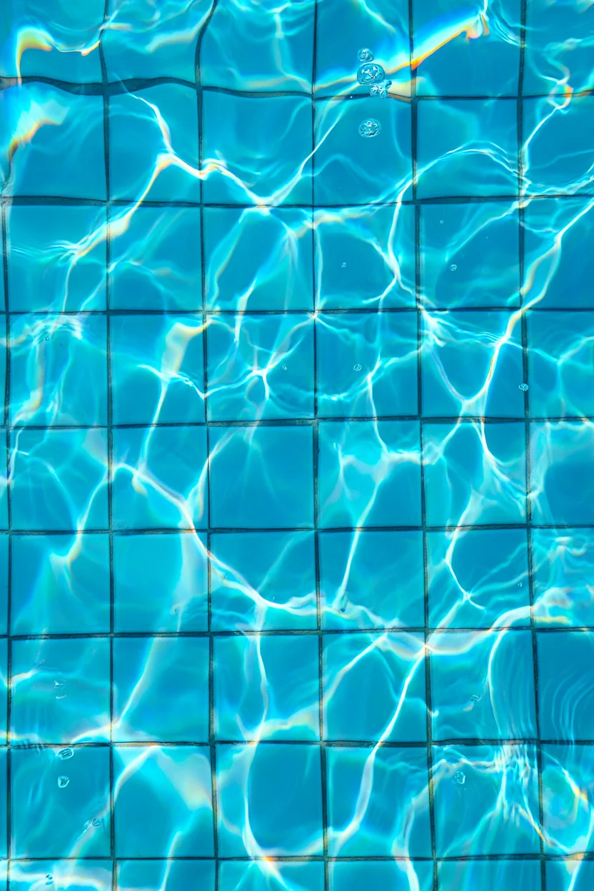 A pool scene captured from below the water's surface, looking up at a grid of light blue ceramic tiles. The tiles are distorted by rippling water, creating a wavy, refracted pattern characteristic of y2k-era digital aesthetics. Light streaming through the water casts shimmering cyan reflections across the tiles, while small air bubbles rise toward the surface. The underwater perspective emphasizes the geometric patterns of the square tiles arranged in neat rows and columns. Digital photography with heavy color saturation and chromatic aberration effects typical of early 2000s editing techniques.